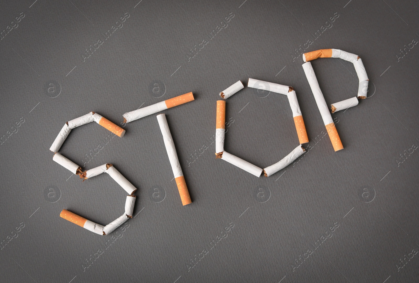 Photo of Word Stop made of cigarettes on dark grey background, top view. Quitting smoking concept
