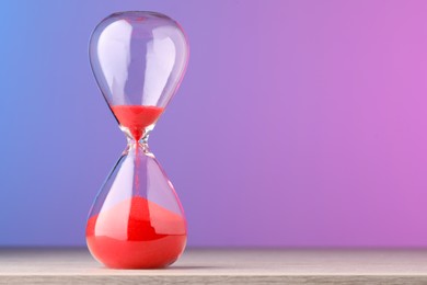 Photo of Hourglass with flowing red sand on table against color background, space for text