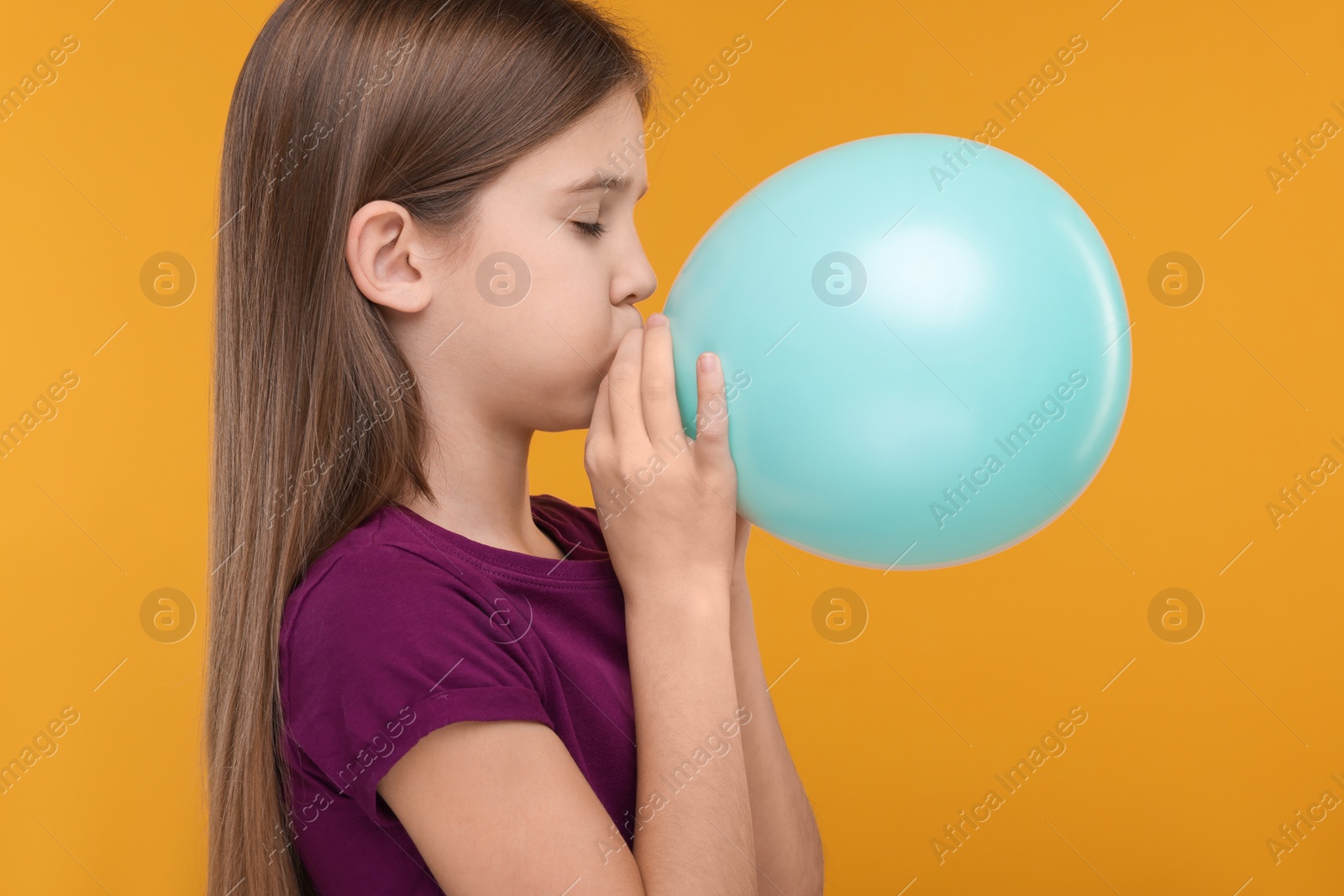 Photo of Girl inflating bright balloon on orange background