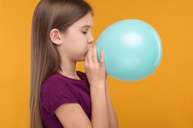 Photo of Girl inflating bright balloon on orange background