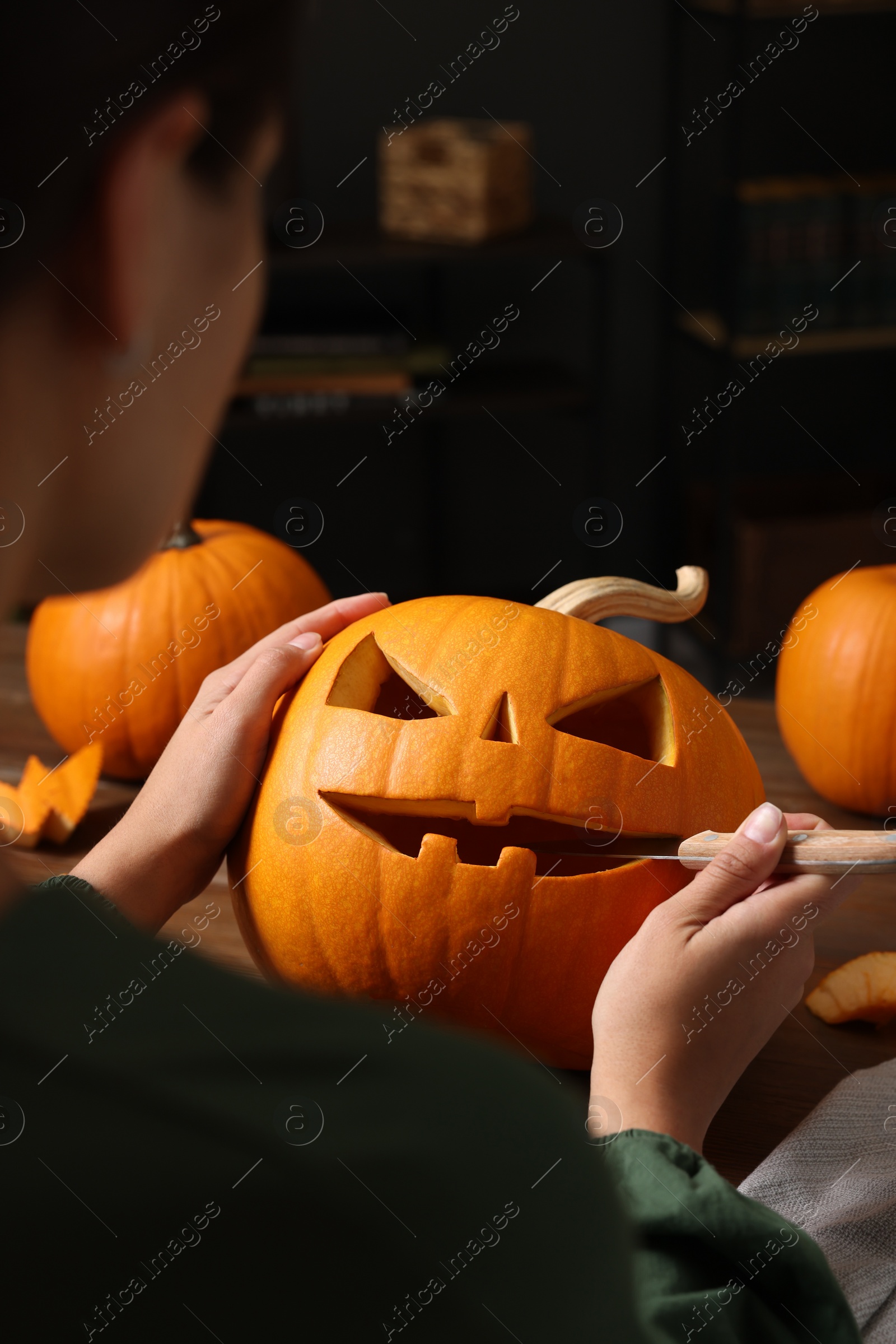 Photo of Woman carving pumpkin for Halloween at wooden table, closeup