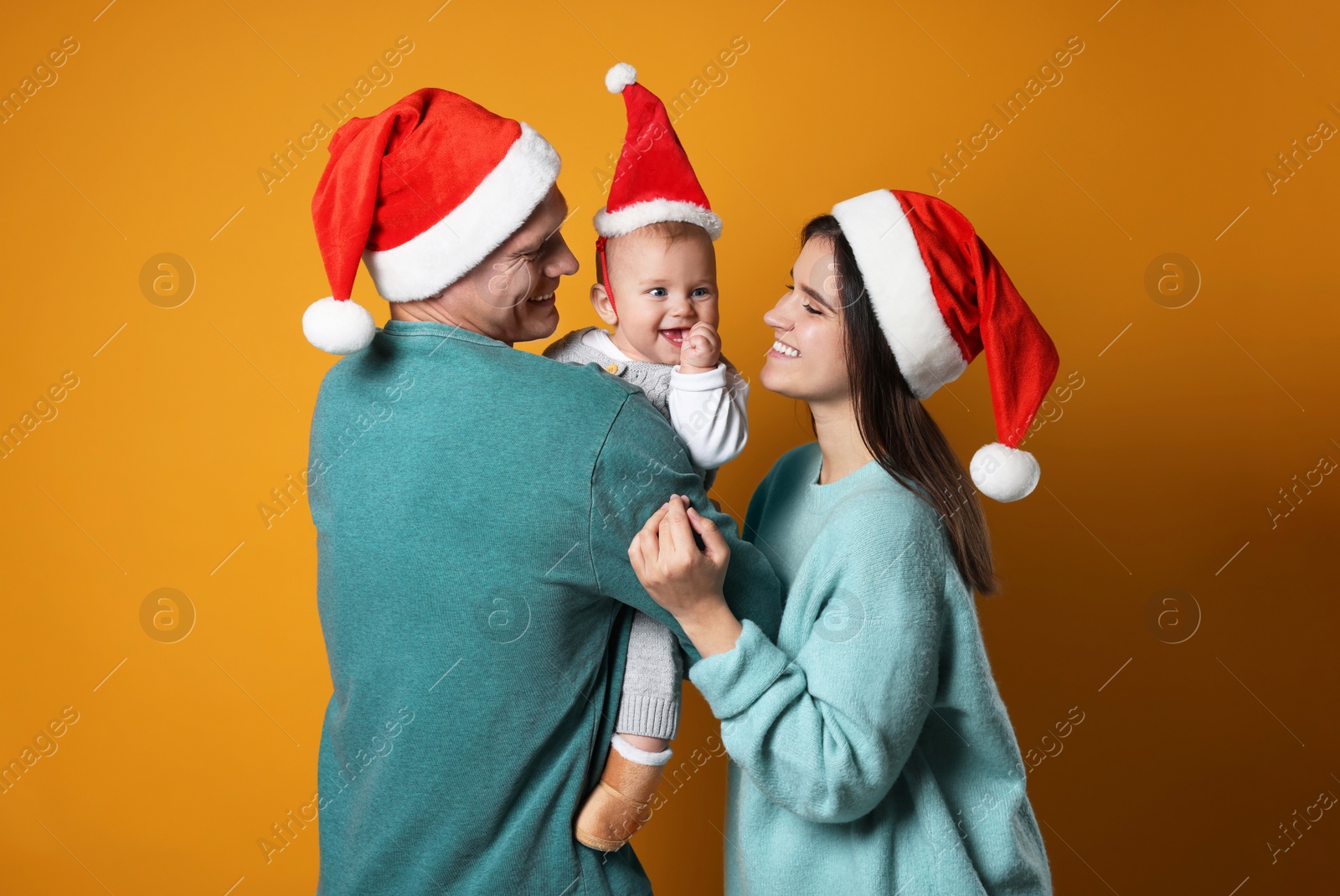 Photo of Happy couple with cute baby wearing Santa hats on yellow background. Christmas season