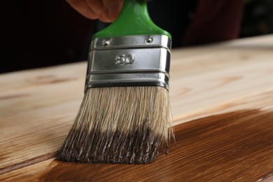 Photo of Man applying wood stain onto wooden surface, closeup