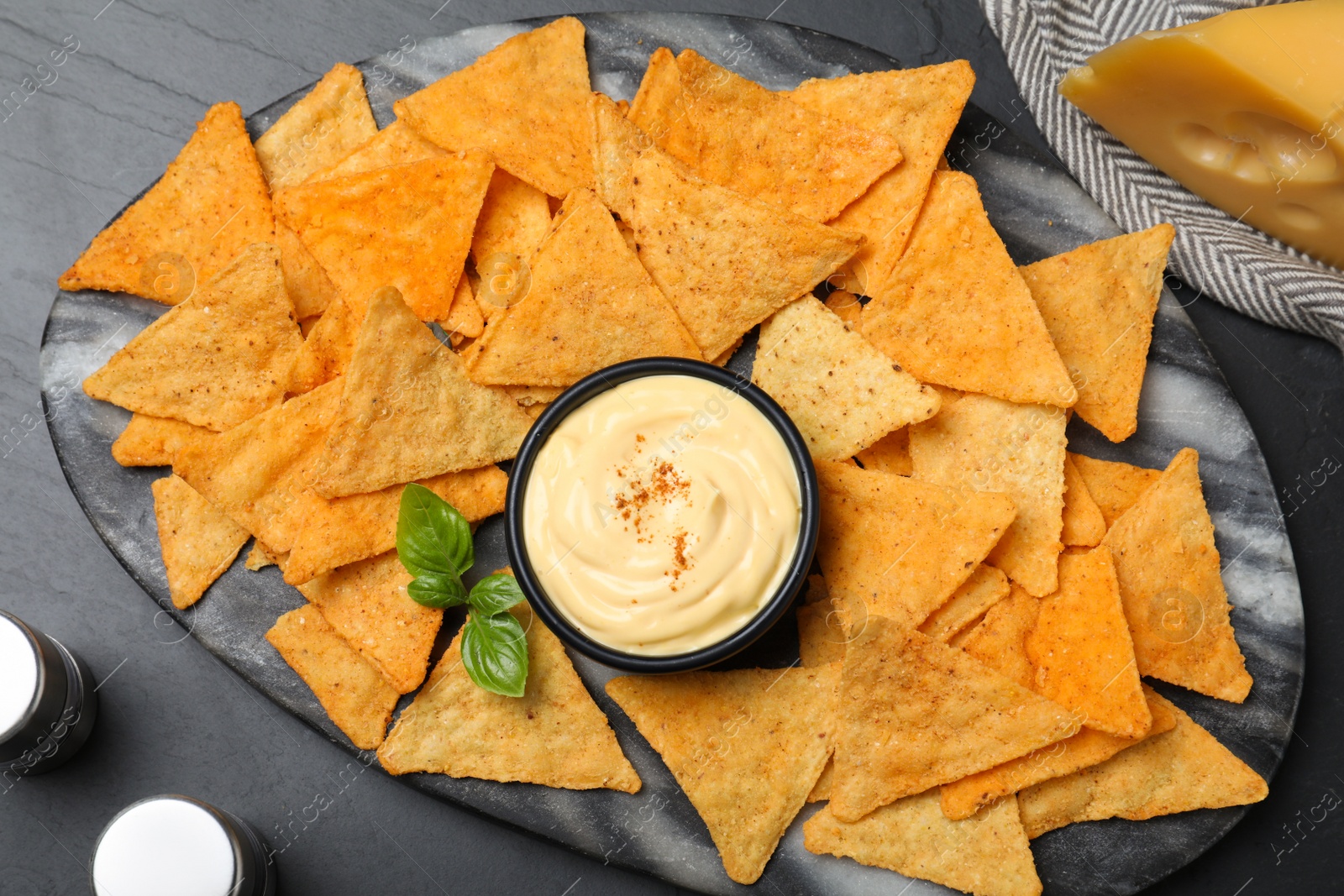 Photo of Delicious nachos and cheese sauce with basil on black table, flat lay
