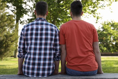Photo of Gay couple sitting on bench in park, back view