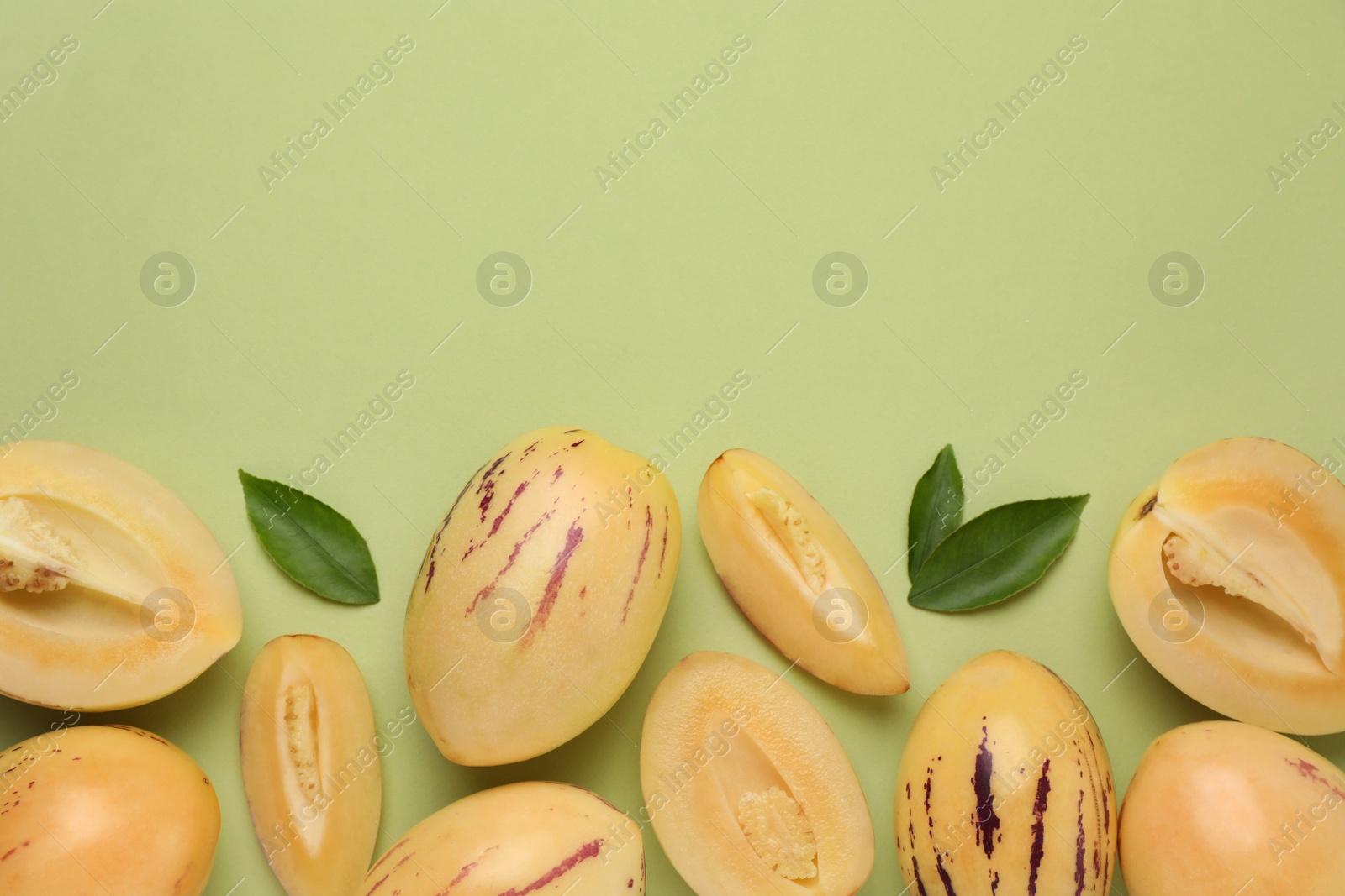Photo of Whole and cut pepino melons with fresh leaves on green background, flat lay. Space for text