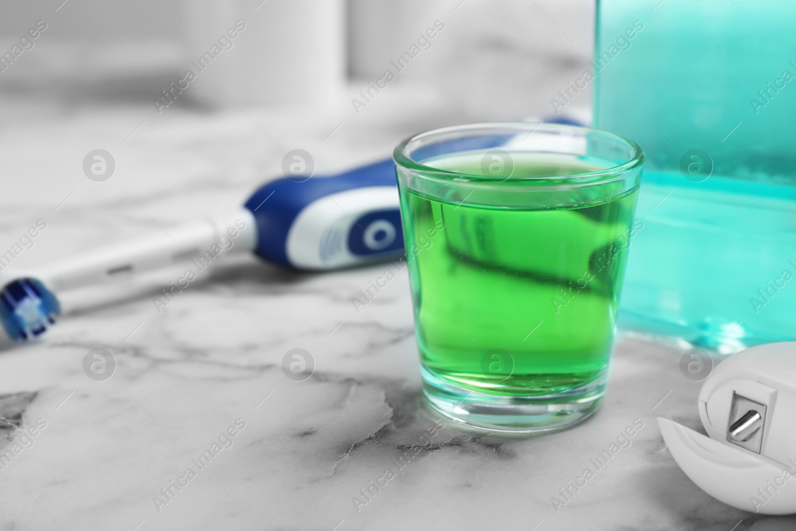 Photo of Glass with mouthwash on marble table. Teeth care