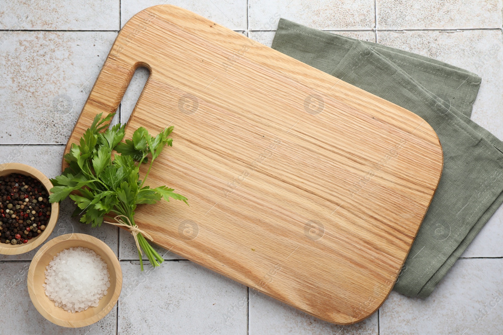 Photo of Cutting board, salt, pepper and parsley on white tiled table, flat lay. Space for text