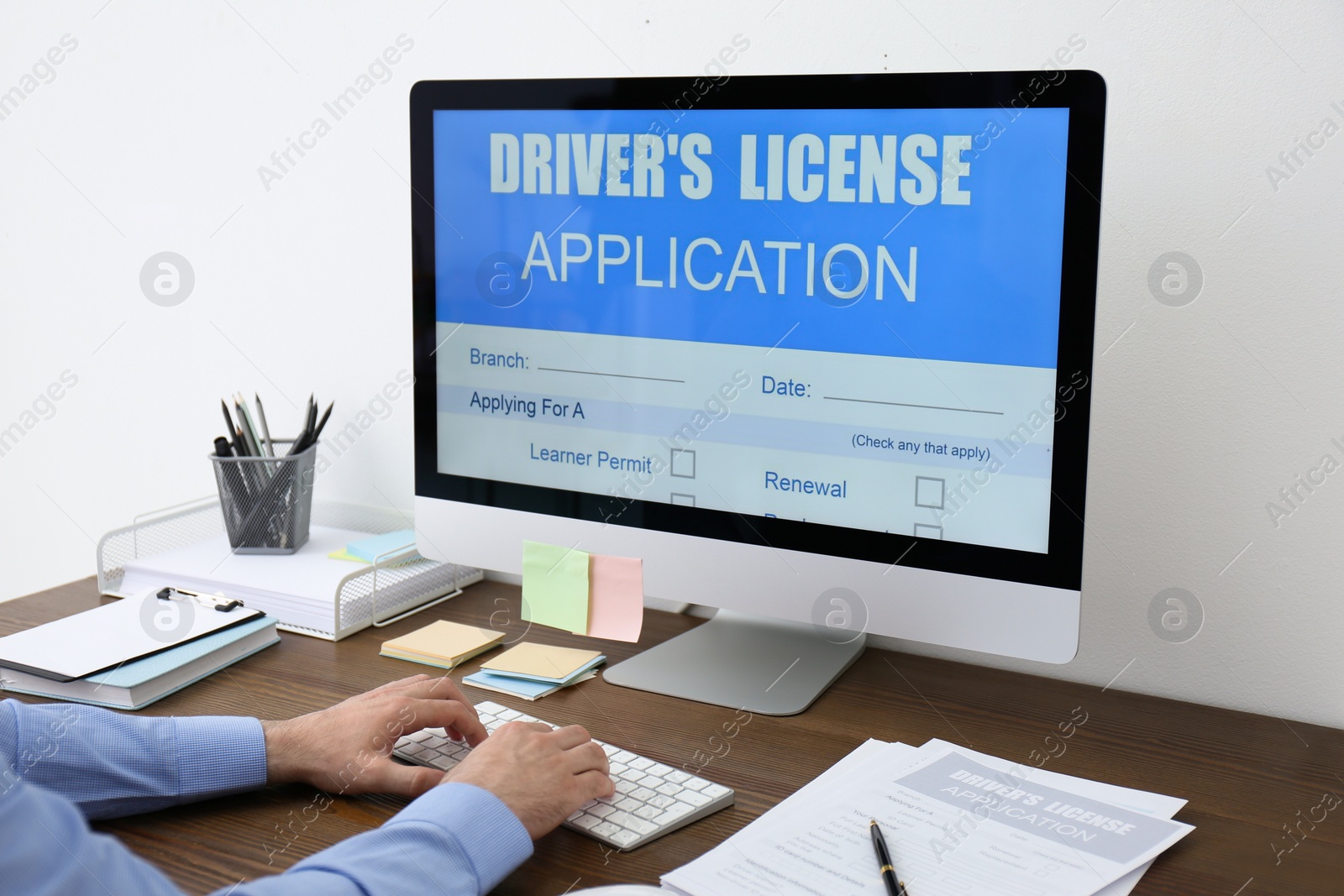 Photo of Man using computer to fill driver's license application form at table in office, closeup