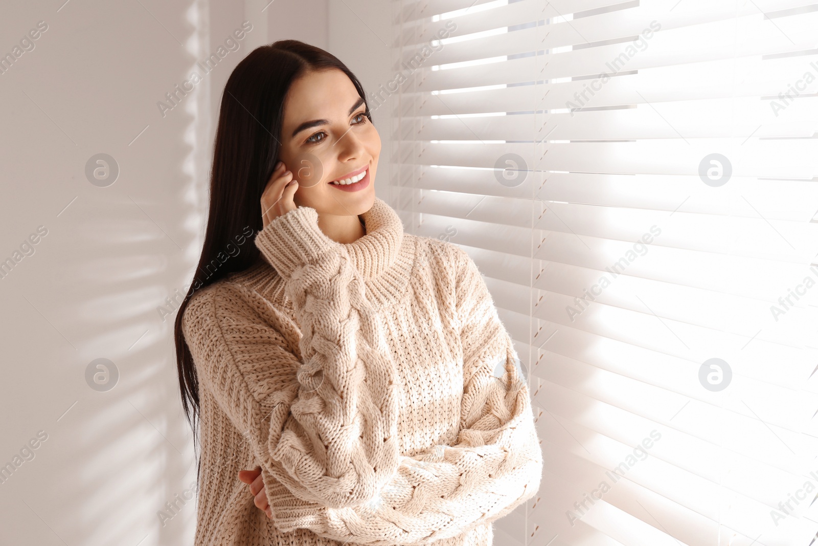 Photo of Young woman wearing warm sweater near window at home. Winter season