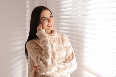 Photo of Young woman wearing warm sweater near window at home. Winter season