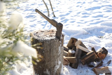 Photo of Metal axe in wooden log outdoors on sunny winter day