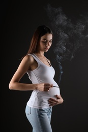Photo of Pregnant woman smoking cigarette on black background