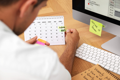 Photo of Man putting sticker on calendar at table in office, closeup