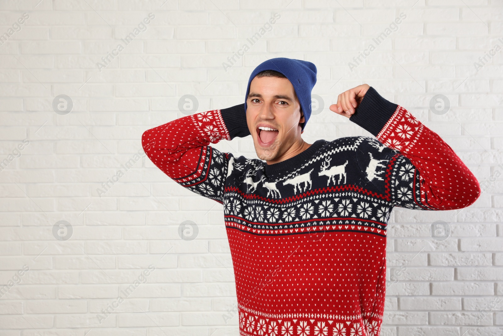 Photo of Portrait of man in Christmas sweater and hat near white brick wall