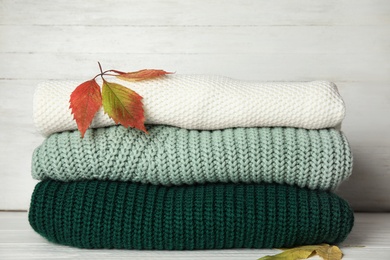 Photo of Stack of warm knitted clothes and autumn leaves on white wooden background