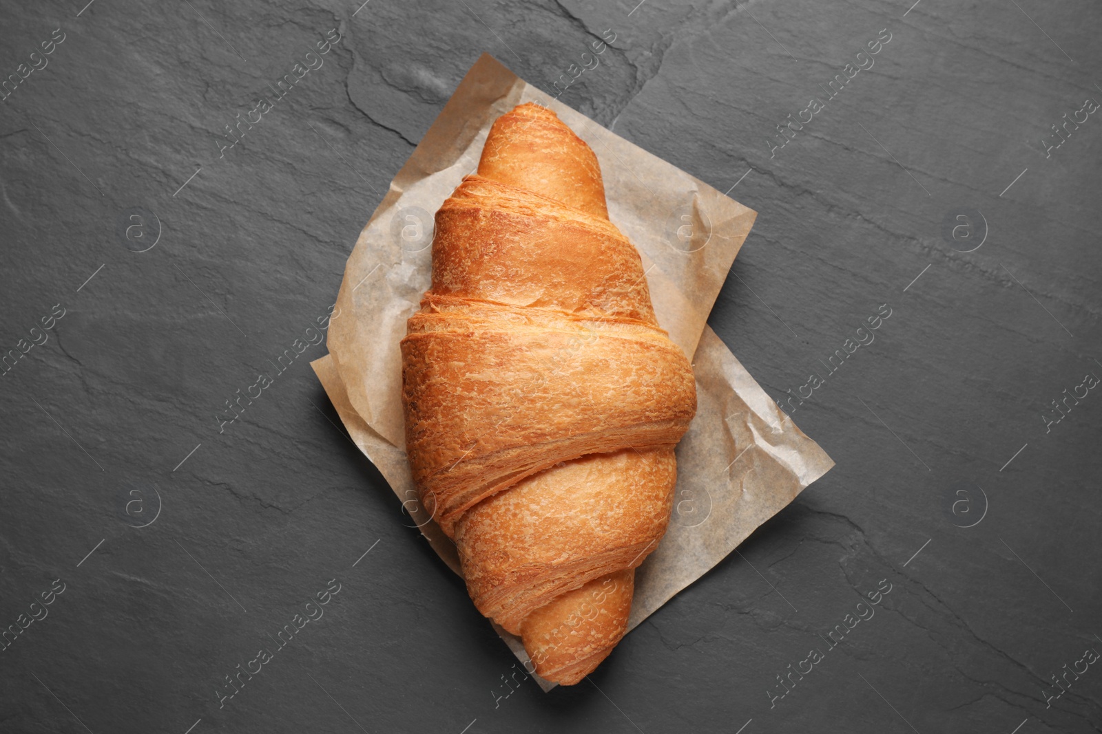 Photo of Tasty fresh croissant on black table, top view