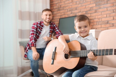 Photo of Father watching his son playing guitar at home