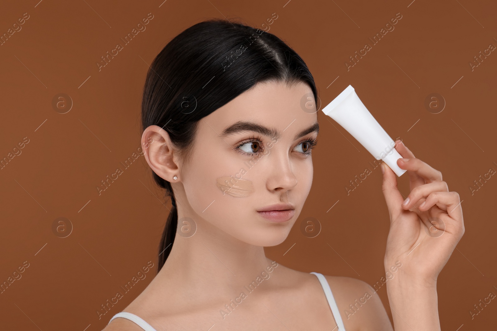 Photo of Teenage girl holding tube with foundation on brown background