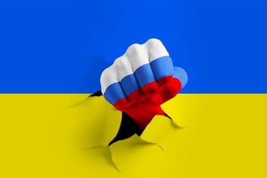 Image of Russian invasion of Ukraine. Man breaking through paper Ukrainian flag with fist painted in colors of Russian flag