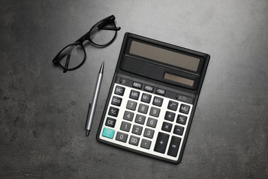 Calculator, glasses and pen on dark gray table, flat lay