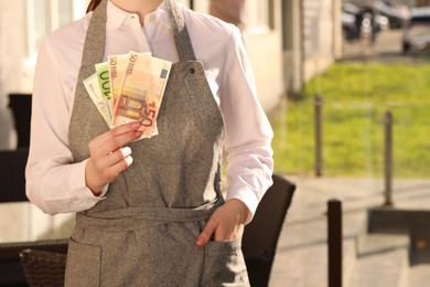 Waitress holding payment for order and tips at outdoor cafe, closeup