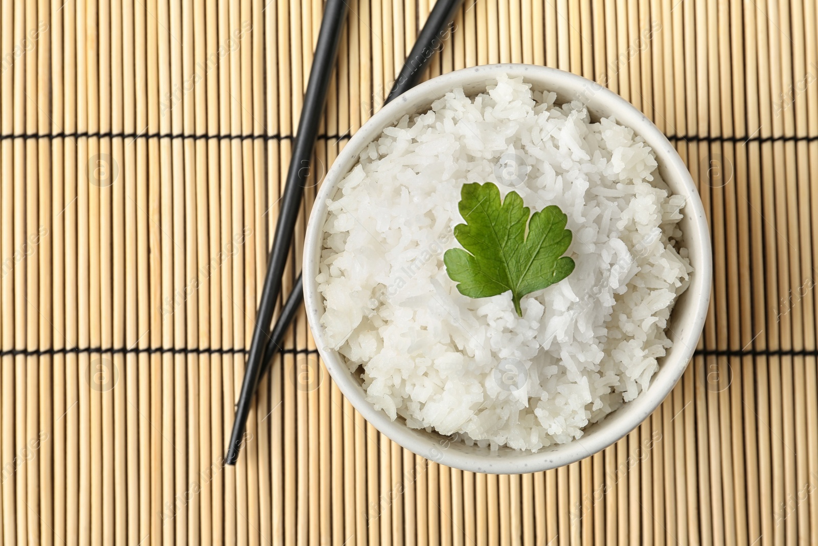 Photo of Boiled rice in bowl and chopsticks on bamboo mat, top view with space for text