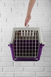 Photo of Woman holding violet pet carrier near white brick wall, closeup