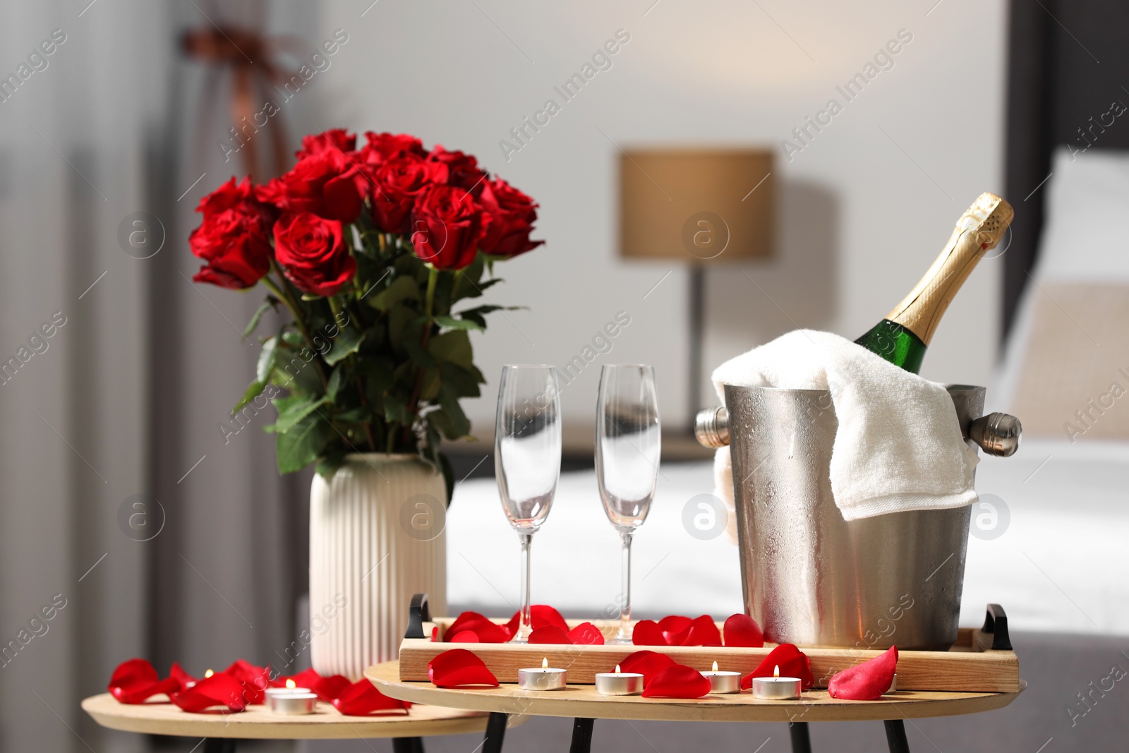 Photo of Honeymoon. Sparkling wine, glasses and bouquet of roses on wooden table in room