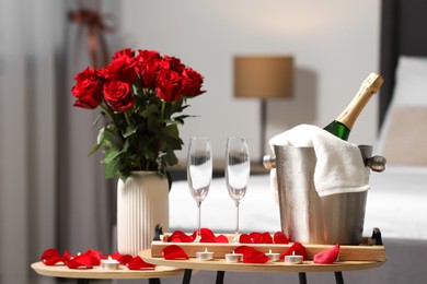 Honeymoon. Sparkling wine, glasses and bouquet of roses on wooden table in room