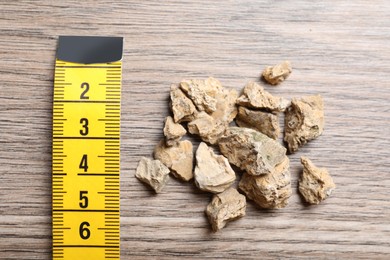 Pile of kidney stones and measuring tape on wooden table, flat lay