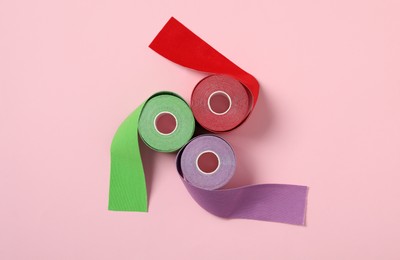 Photo of Bright kinesio tape in rolls on pink background, flat lay
