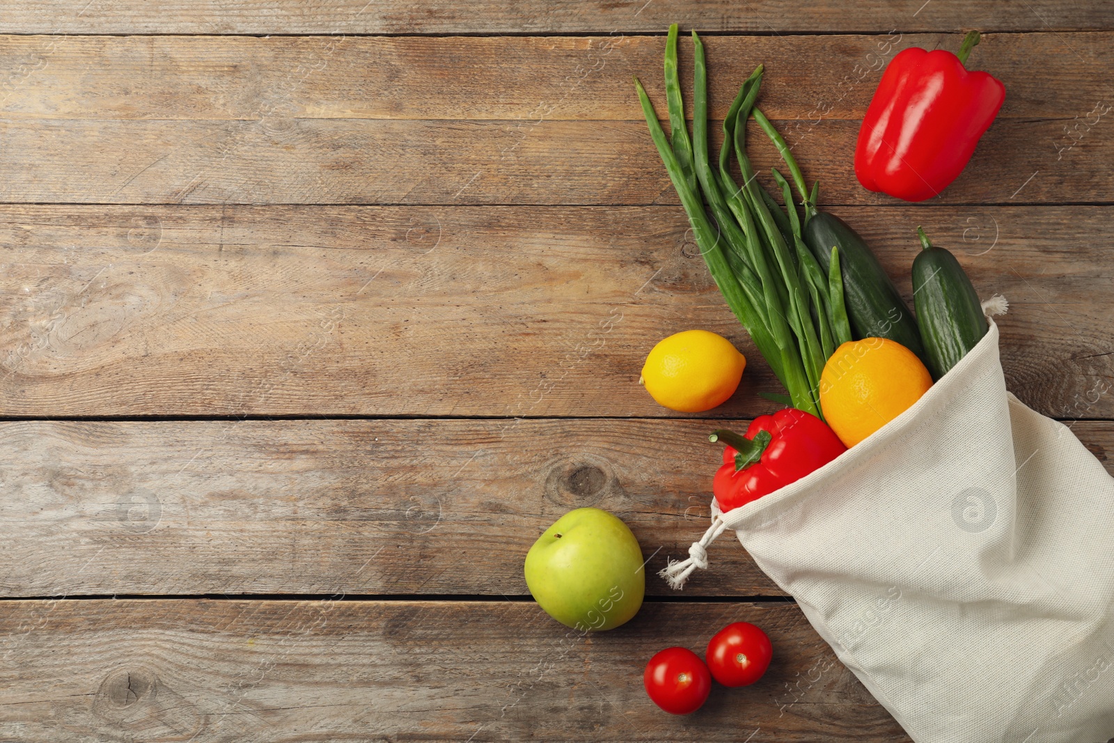 Photo of Cotton eco bag with vegetables and fruits on wooden table, flat lay. Space for text