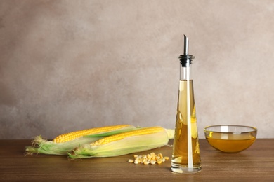 Photo of Bottle with fresh corn oil and cobs on table against color wall