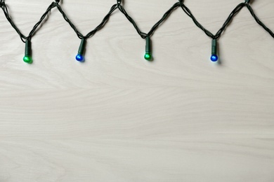 Photo of Beautiful glowing Christmas lights on white wooden background, top view. Space for text