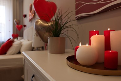 Photo of Burning candles on white table in room decorated for Valentine's Day