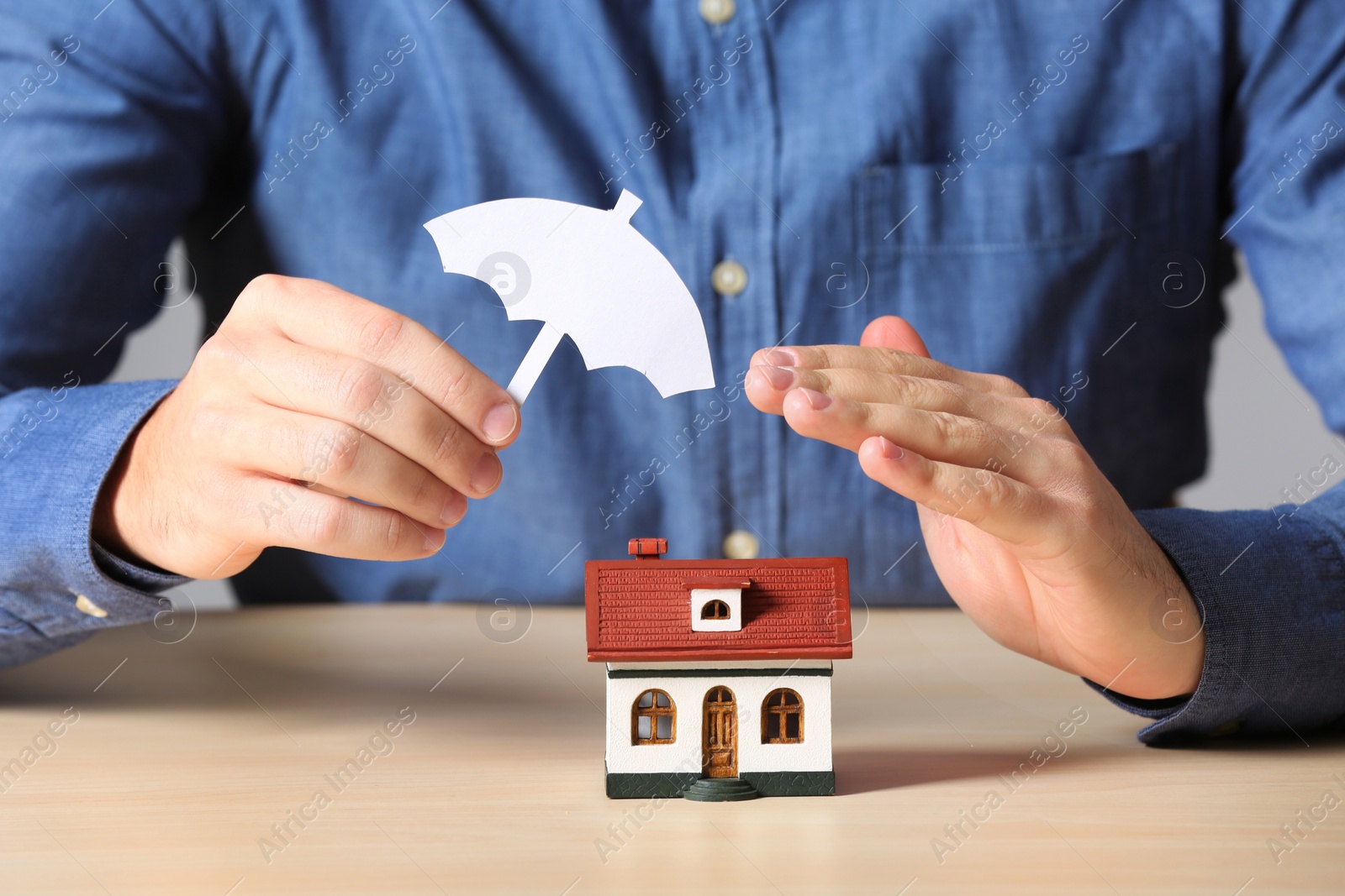 Photo of Man covering house model with umbrella cutout at table, closeup. Home insurance