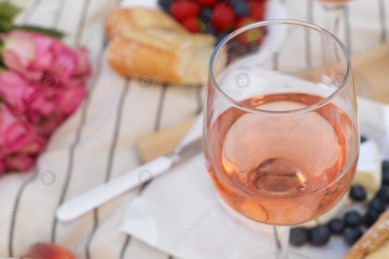 Photo of Glass of delicious rose wine and food on white picnic blanket, closeup