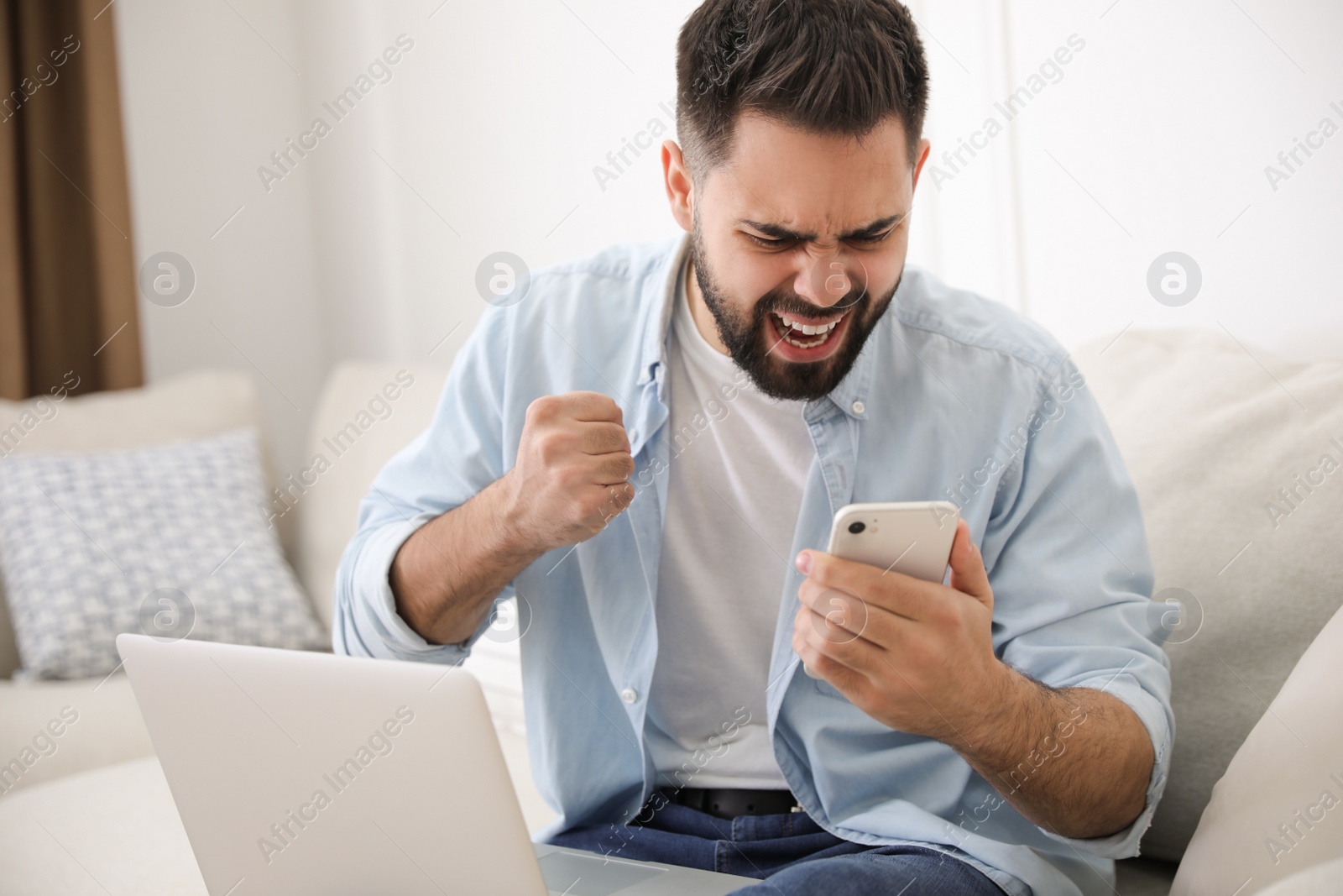 Photo of Emotional young man with laptop and smartphone at home. Online hate concept