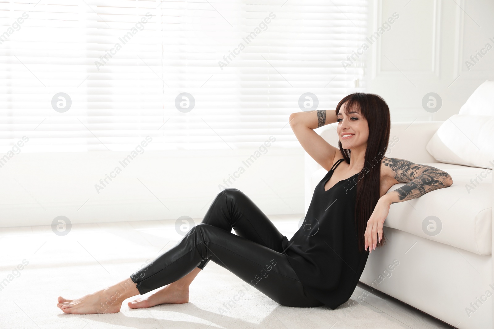 Photo of Beautiful woman with tattoos on arms resting in living room