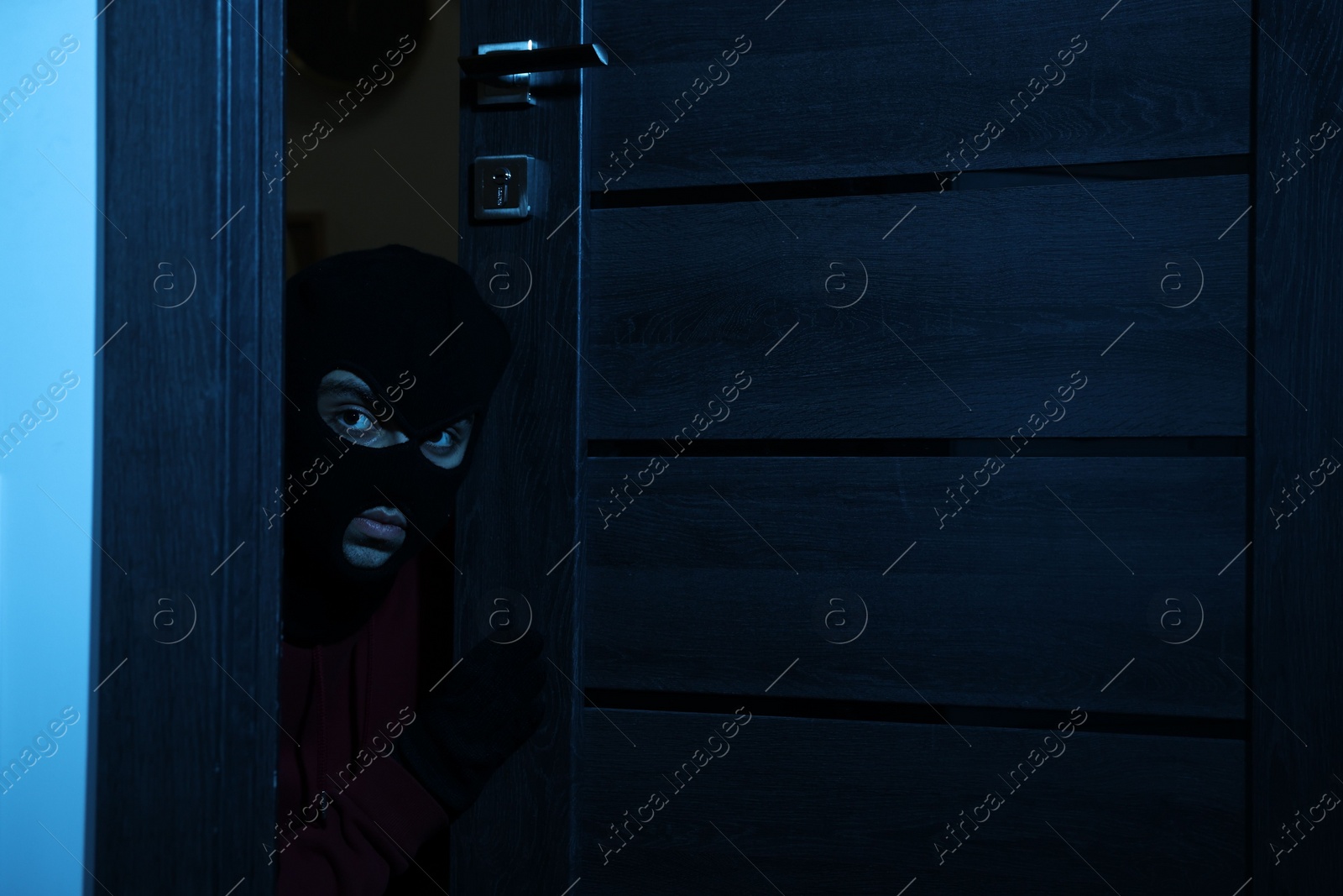 Photo of Thief in balaclava entering foreign house at night. Burglary