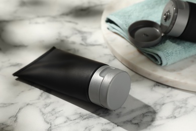 Photo of Men's cosmetic products in black tubes and towel on white marble table, closeup