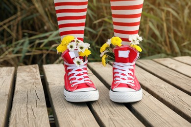 Photo of Woman with beautiful tender flowers in socks on wooden pier, closeup