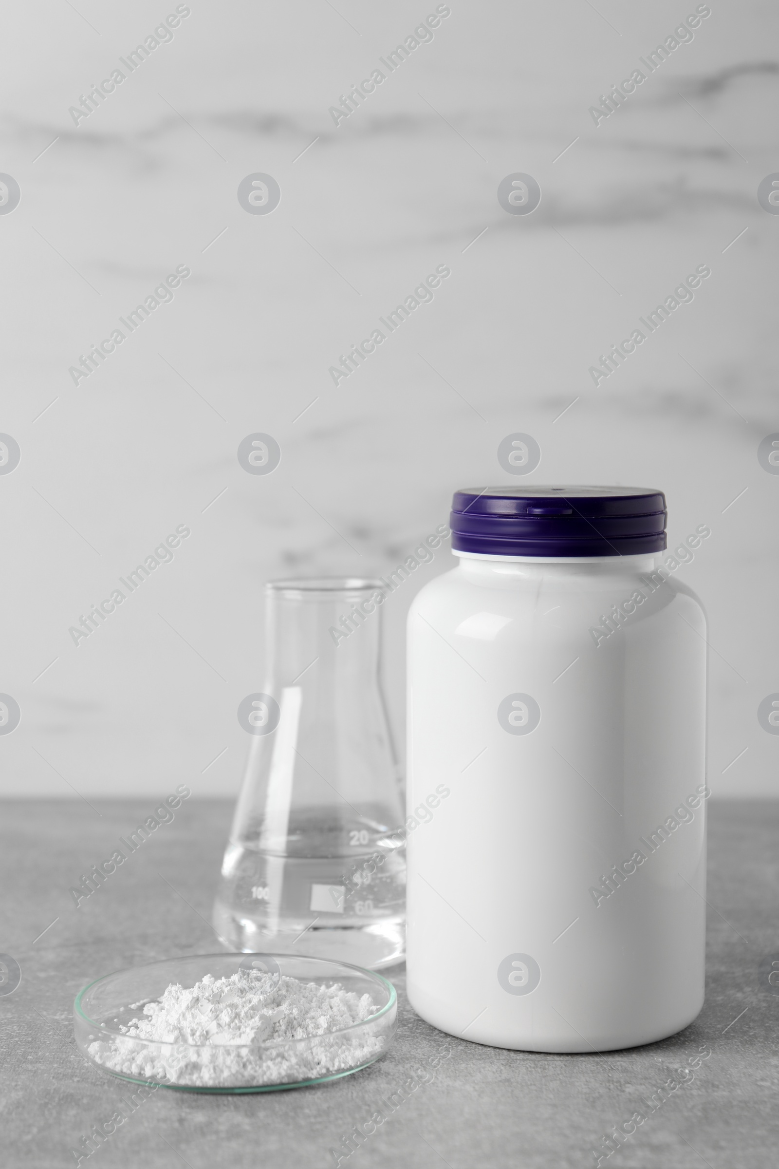 Photo of Petri dish with calcium carbonate powder, jar and laboratory flask on light grey table