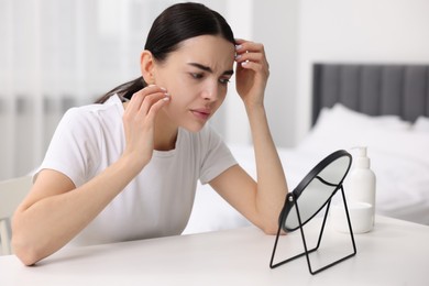 Woman with dry skin looking at mirror indoors