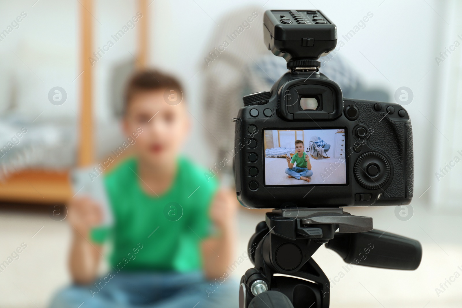 Photo of Cute little blogger with phone and selfie stick recording video at home, focus on camera