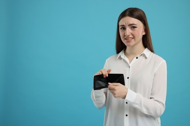 Woman showing empty wallet on light blue background, space for text