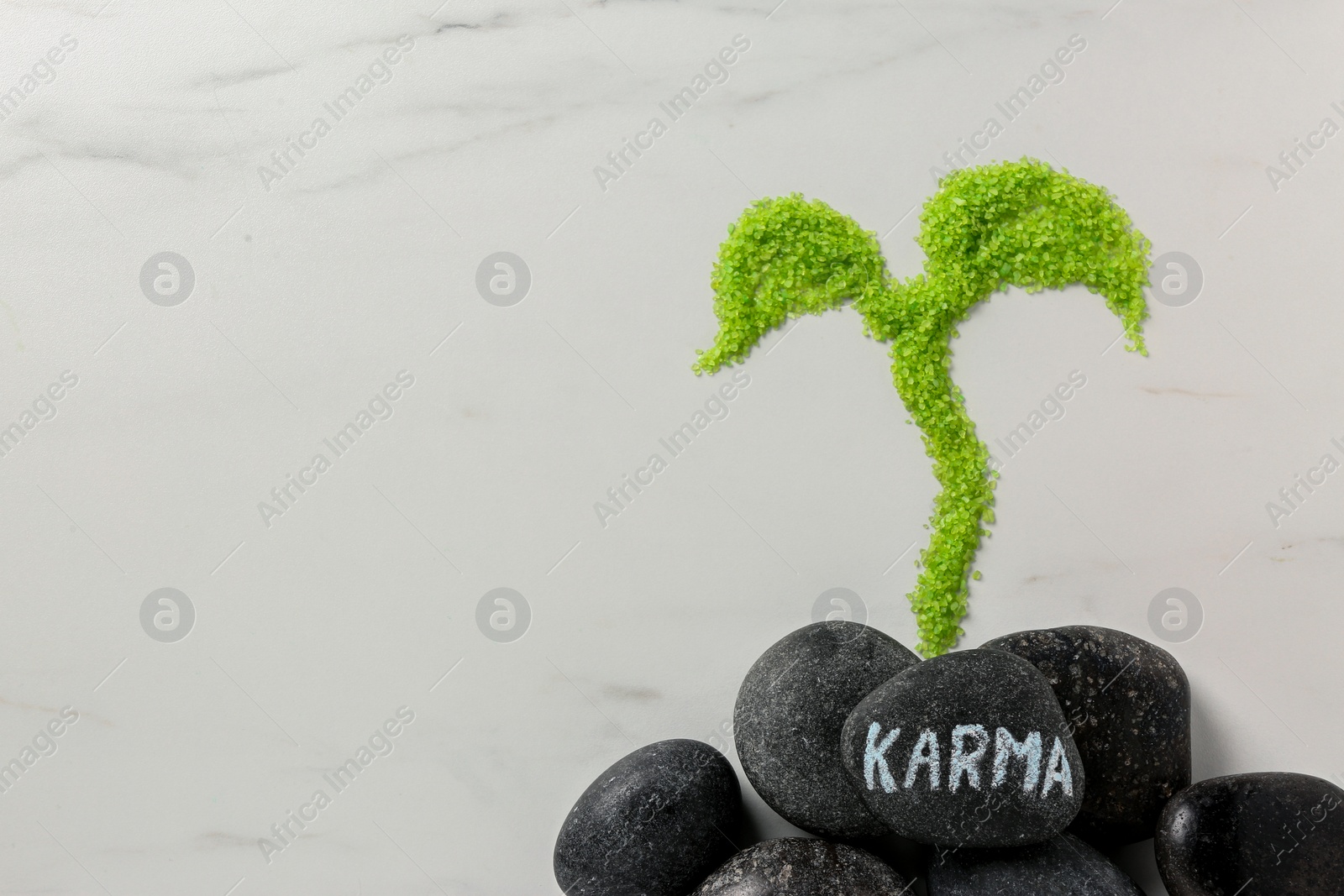 Photo of Stone with word Karma and sprout made of light green sea salt on white marble table, flat lay. Space for text