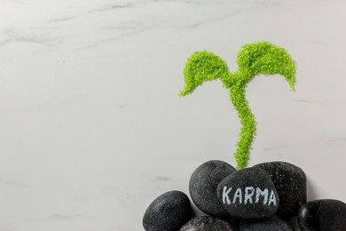 Photo of Stone with word Karma and sprout made of light green sea salt on white marble table, flat lay. Space for text