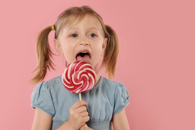 Portrait of cute girl licking lollipop on pink background, space for text